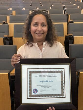 Deepa Dabir holding the framed Rudinica Prize certificate in a lecture hall