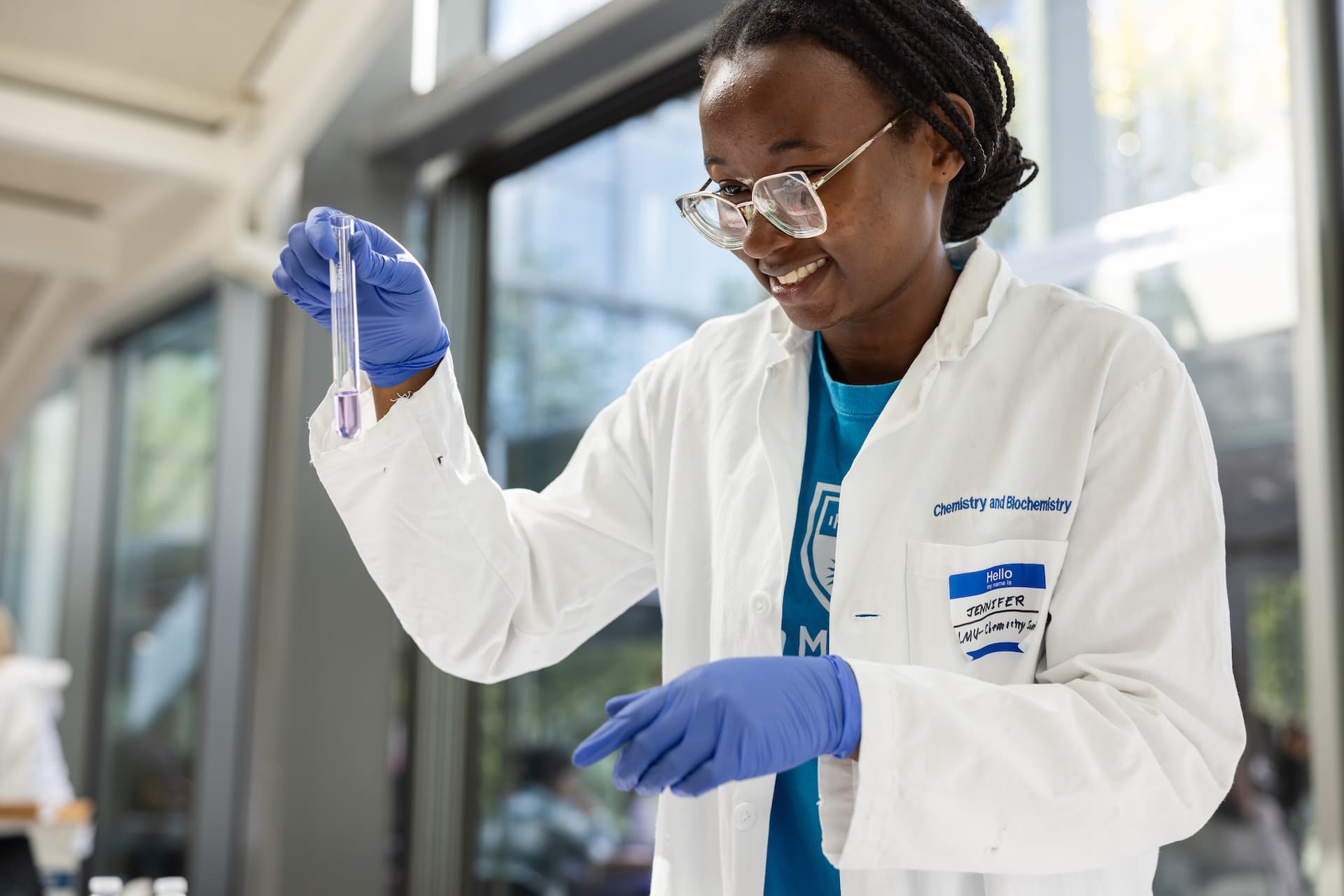 An LMU science student in a lab coat and gloves holding up a test tube